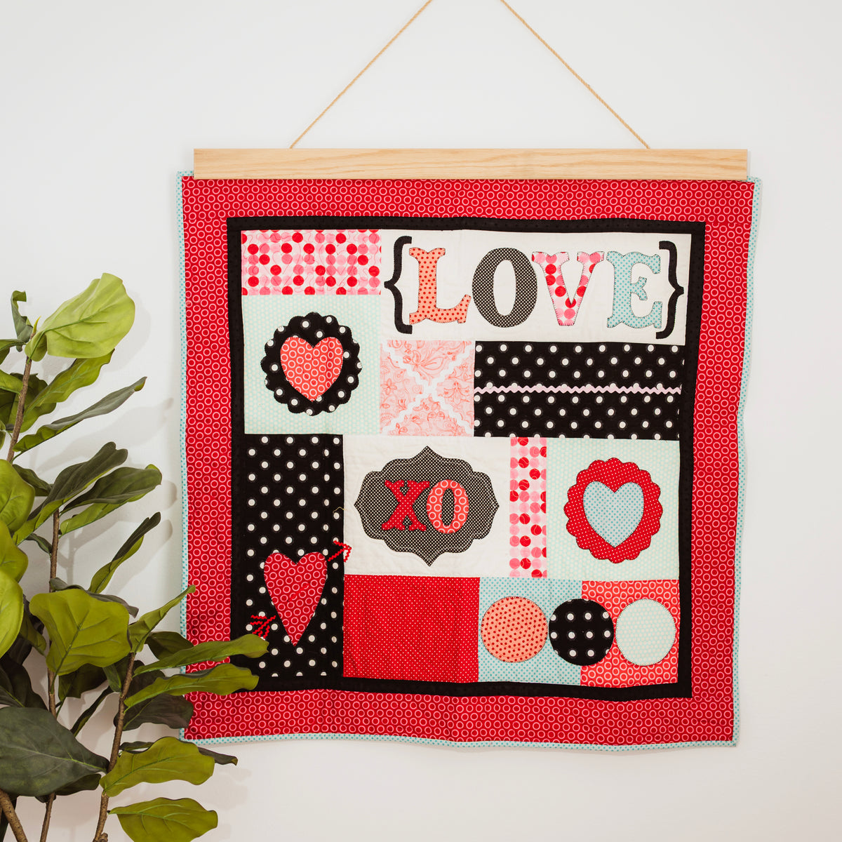 Decorative wall hanging with 'LOVE' and heart designs on a red background, hanging on a white wall. 36" wall hanger