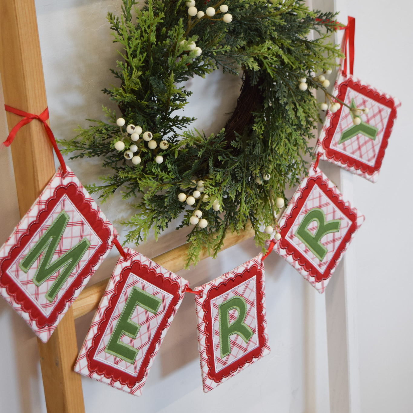 Christmas wreath with 'MERRY' banner on a wooden ladder against a white wall
