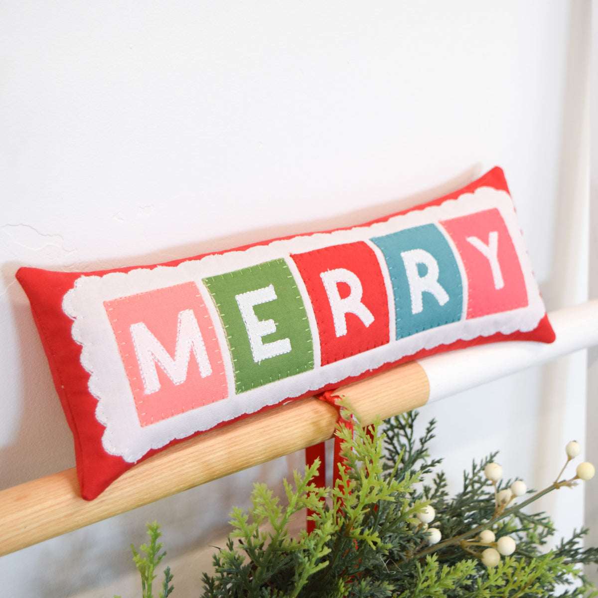 Decorative pillow with 'MERRY' in colorful letters on a white background