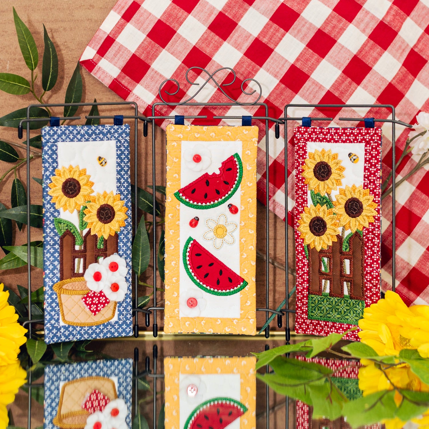 Decorative wall art with sunflowers, watermelons, and a basket on a wooden surface with a red and white checkered cloth in the background.