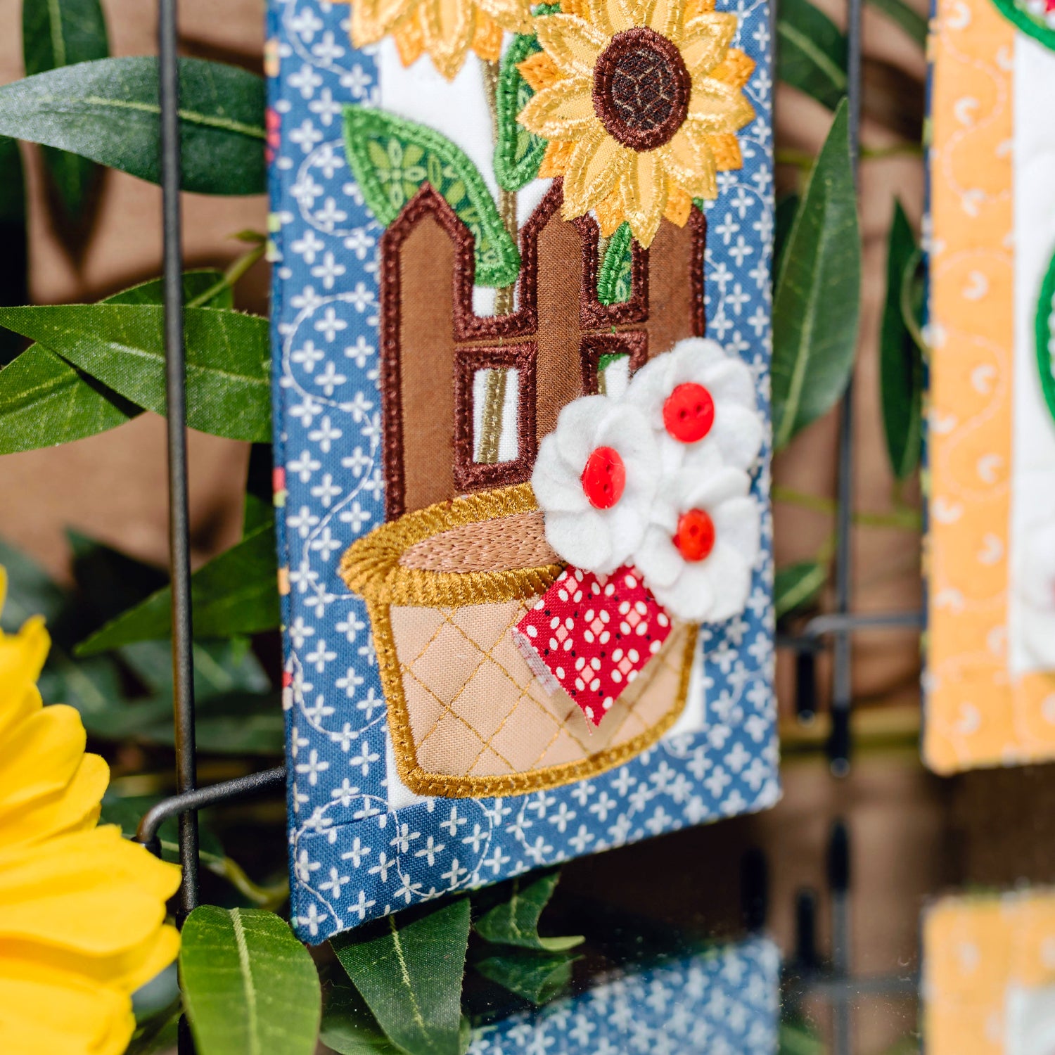 Decorative wall hangings with sunflower, house, and watermelon designs on a blue and yellow background.