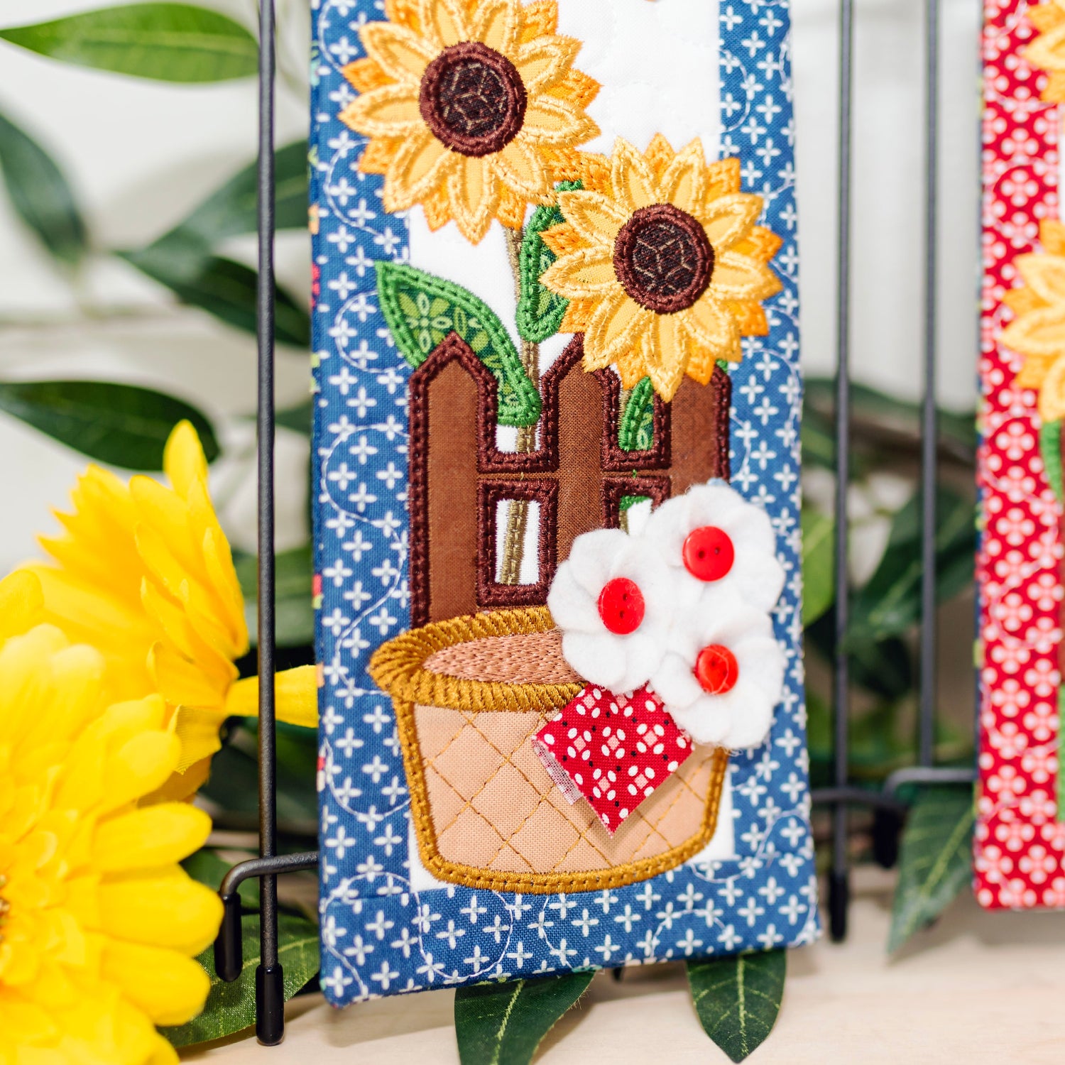 Decorative wall hangings with sunflowers and a basket design on a stand.