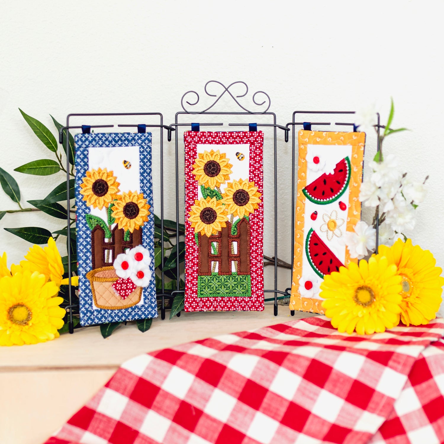 Three decorative panels with sunflower and watermelon designs on a tablecloth with yellow flowers.