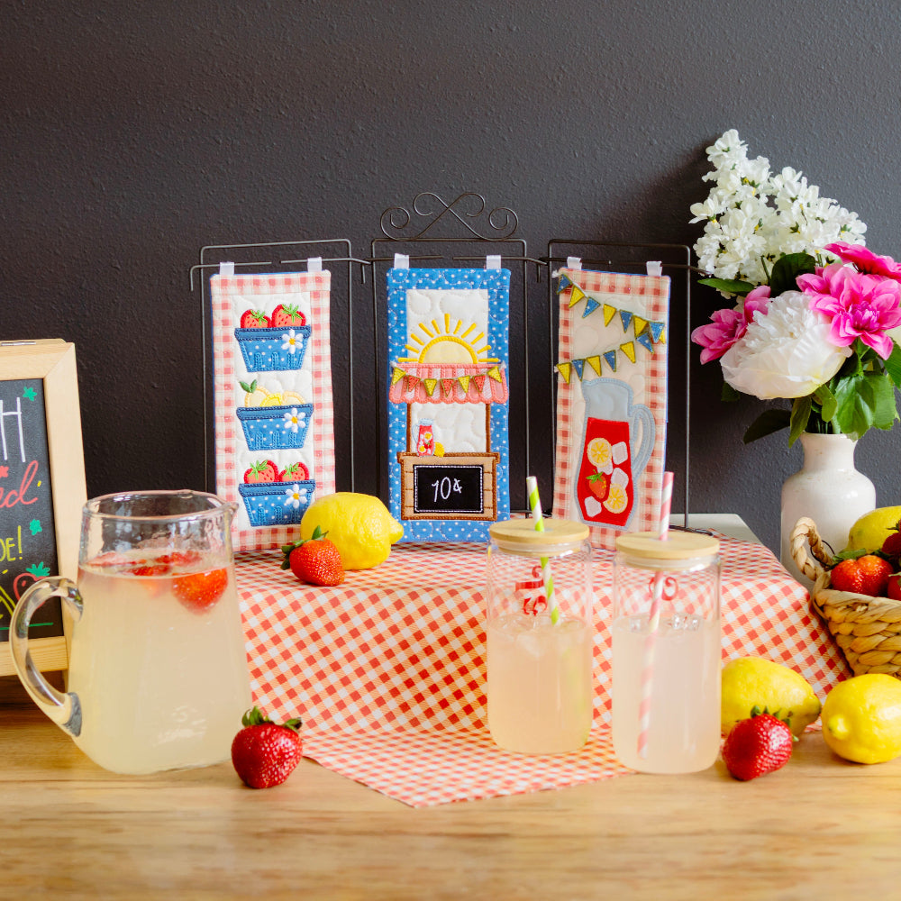 Table setup with lemonade, lemons, strawberries, and decorative elements on a checkered tablecloth.