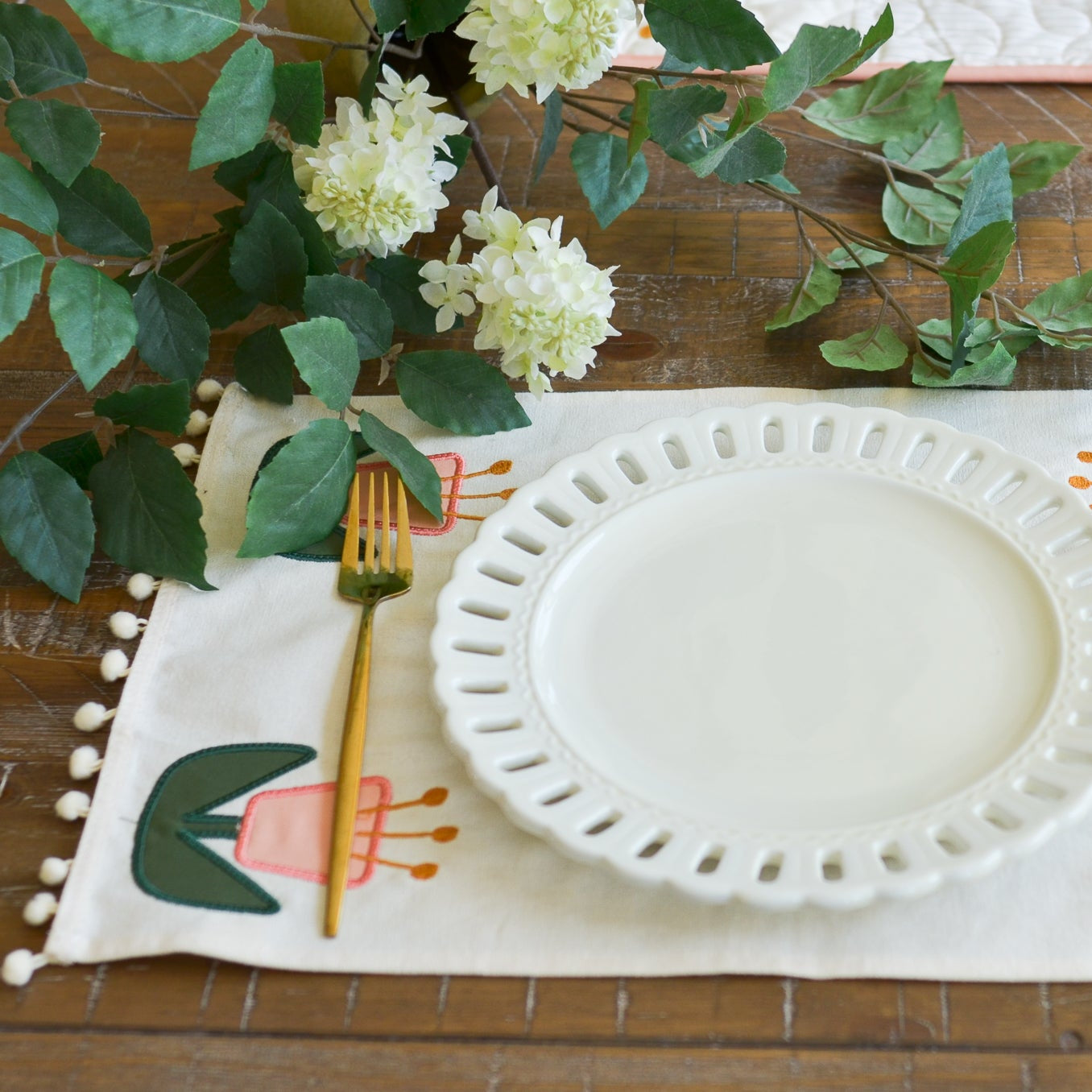 Decorative table setting with a white plate, fork, and spoon on a colorful placemat with floral patterns.