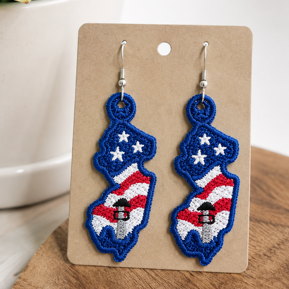 Pair of earrings on a display card with a plant in the background