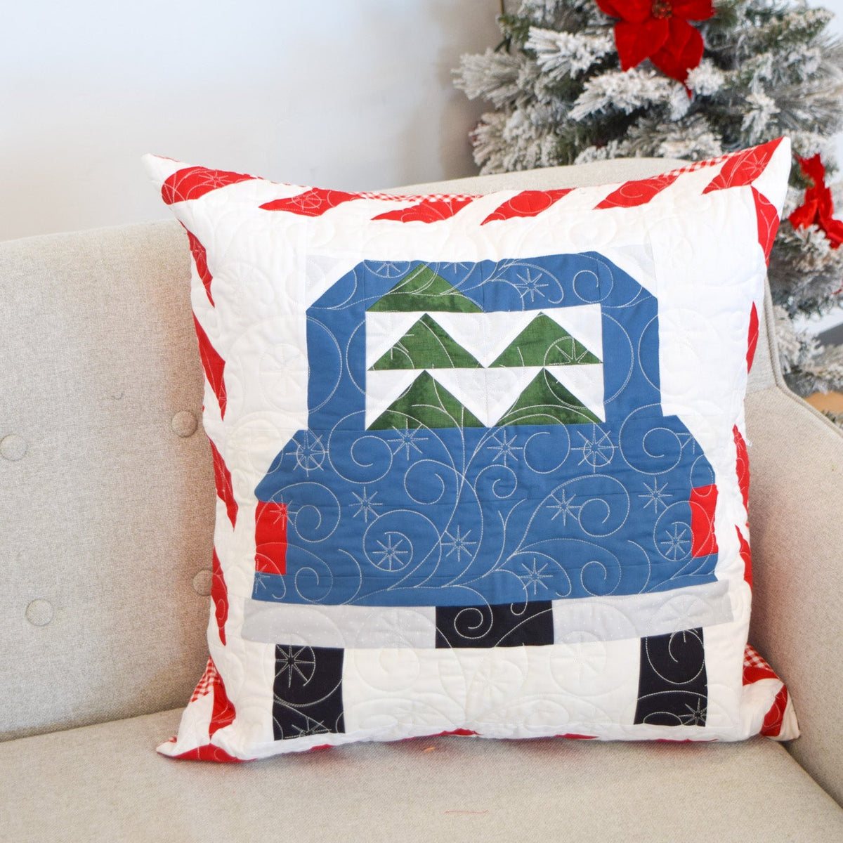 Decorative pillow with a Christmas truck design on a couch next to a decorated tree.