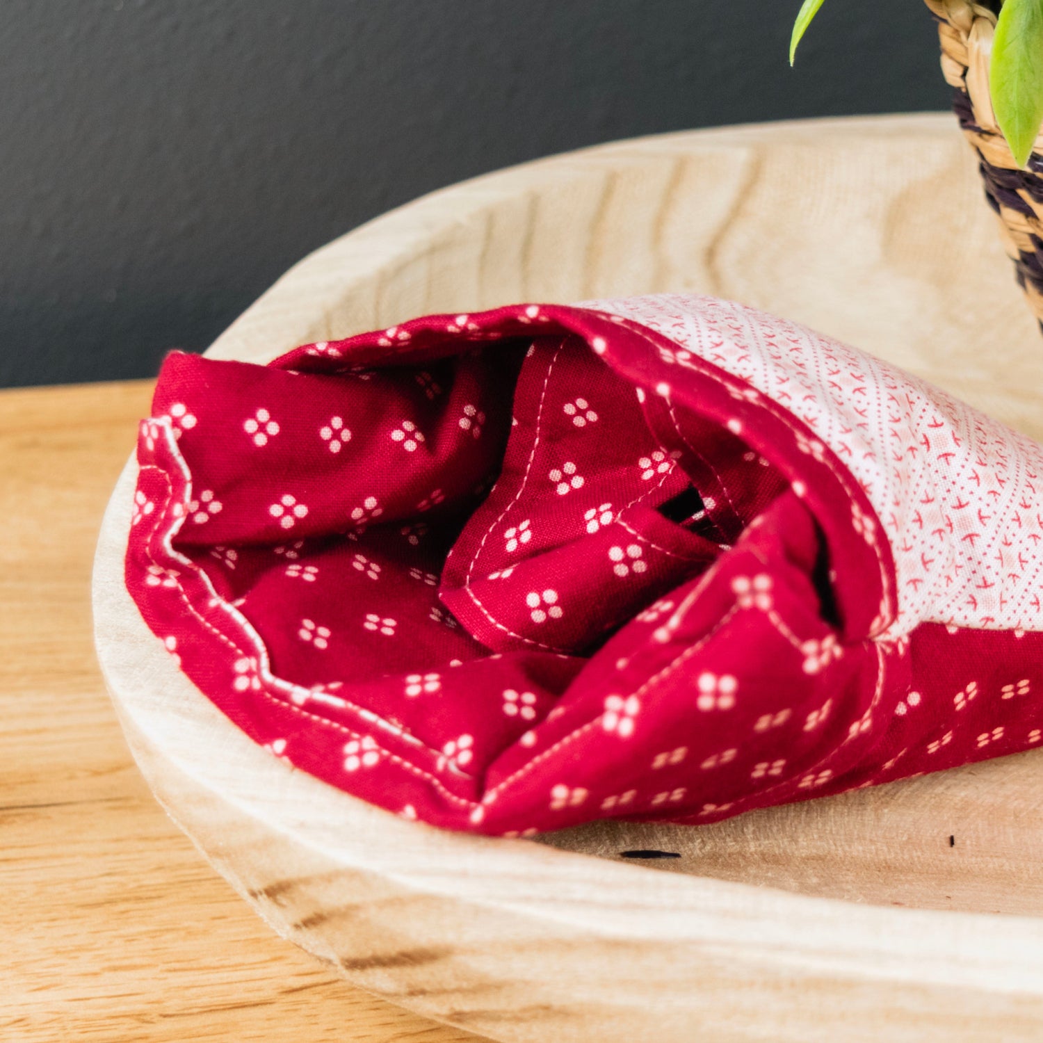 Red patterned fabric rolled up on a wooden surface with a plant in the background