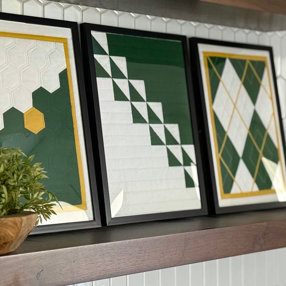 Three framed geometric art pieces on a wooden shelf with a plant.