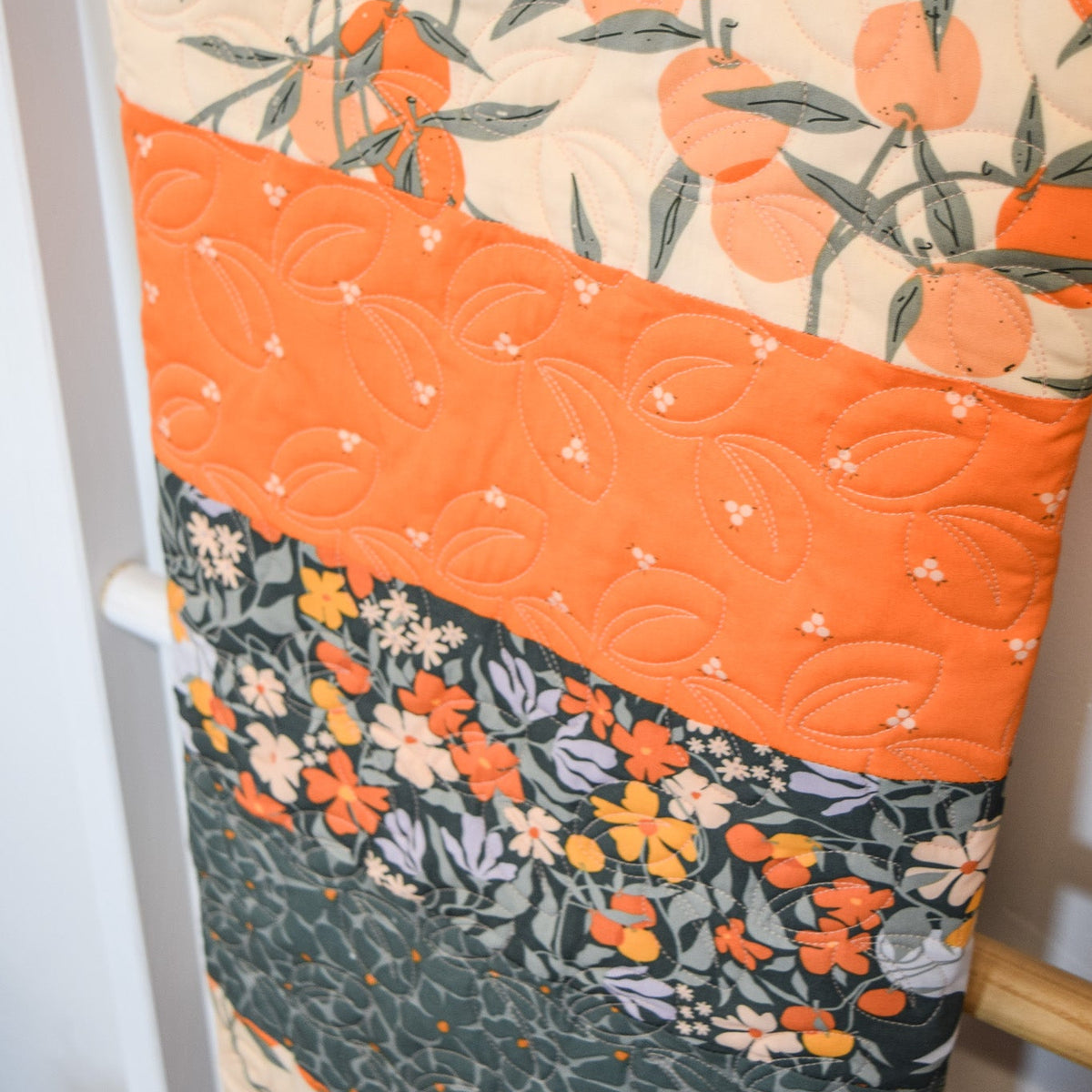 Quilt with floral and fruit patterns draped over a chair.