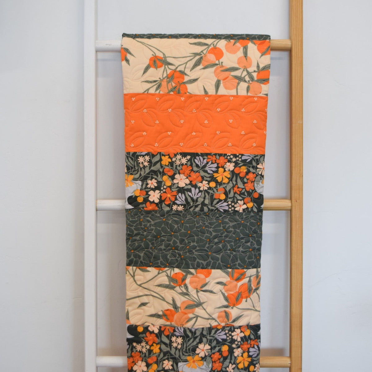 Quilt with floral and fruit patterns draped over a ladder