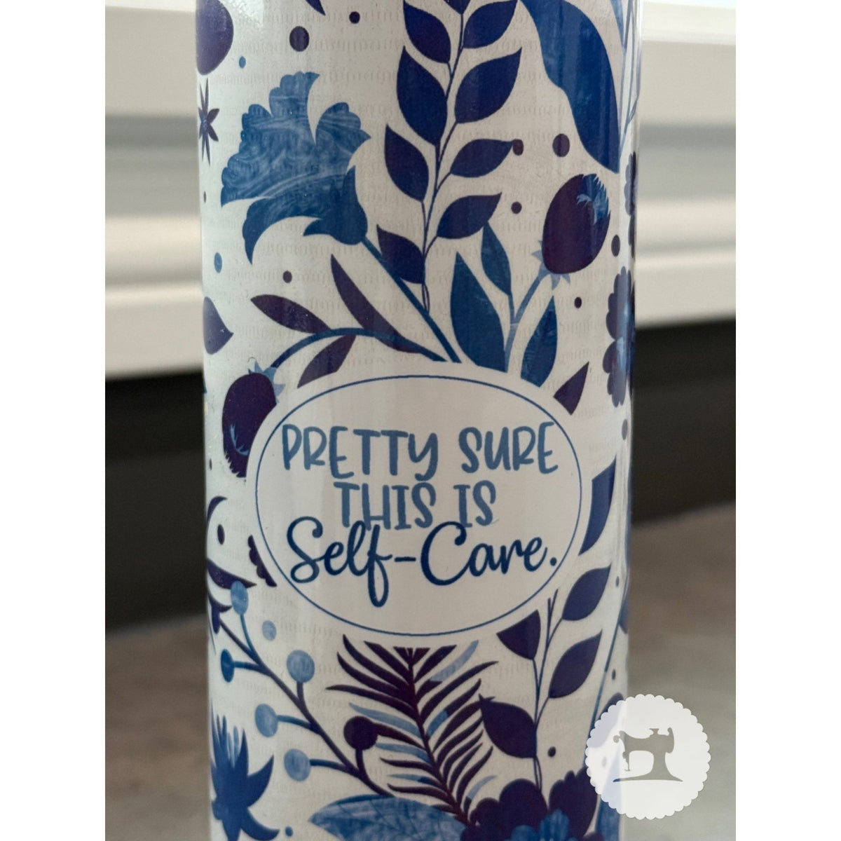 Tumbler with blue floral pattern and 'Pretty sure this is self-care' text on a white background