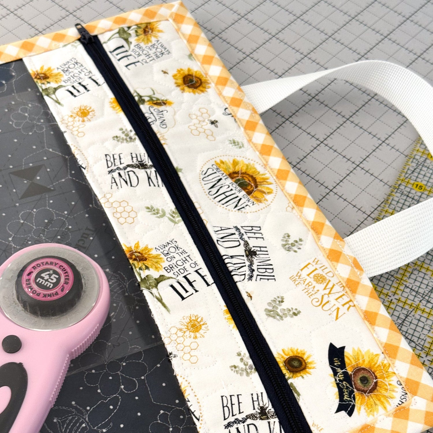 Fabric with sunflower pattern on a cutting mat with a rotary cutter.