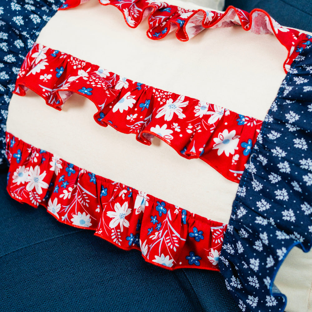 Red, white, and blue floral ruffled fabric on a cushion with a blue background.