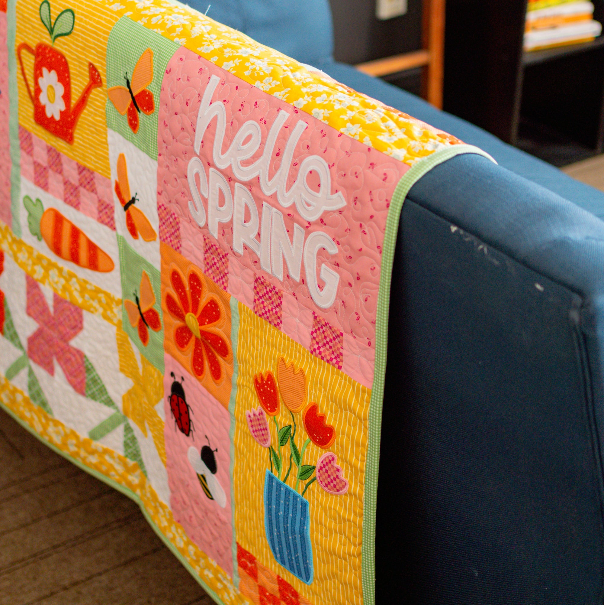 Colorful quilt with 'hello SPRING' text draped over a blue couch.
