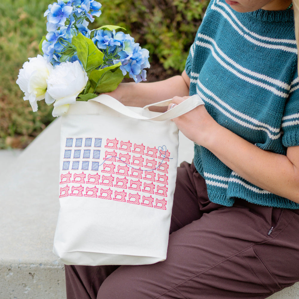 Person holding a tote bag with a pattern and flowers, sitting outdoors.