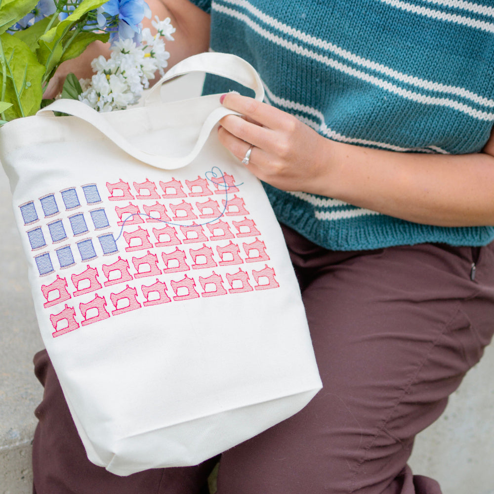 Person holding a tote bag with a pattern, wearing a blue sweater and brown pants.
