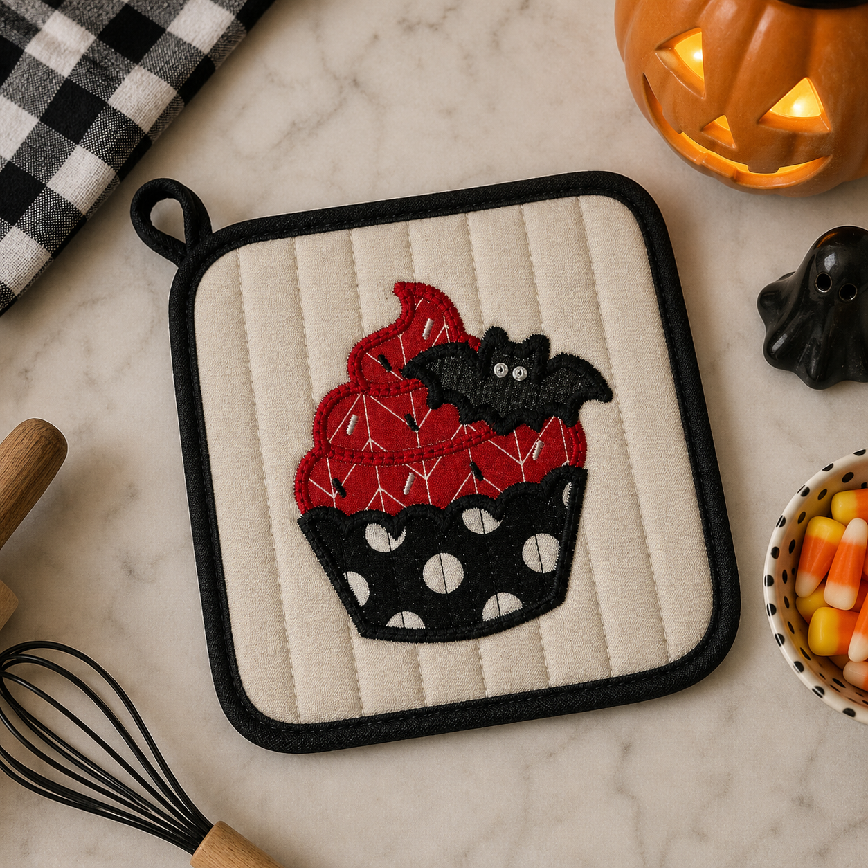 Halloween-themed pot holder with cupcake design on a marble surface.