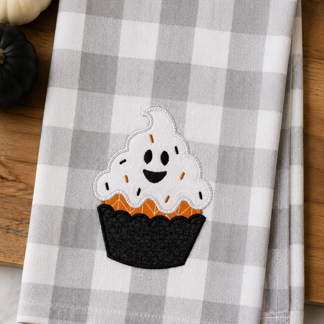Checkered towel with a ghost-themed cupcake design on a wooden surface.