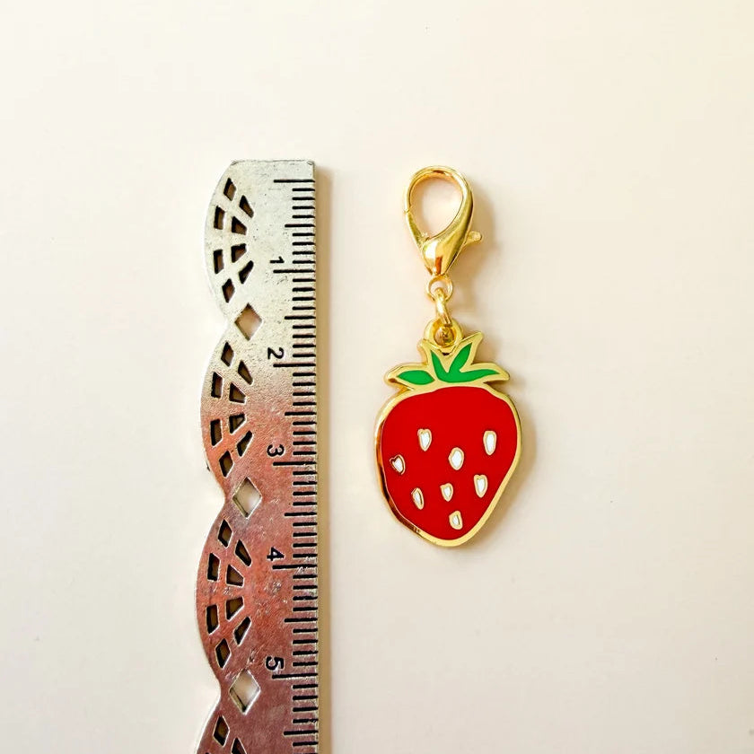 Strawberry-shaped keychain with gold accents next to a ruler on a beige background