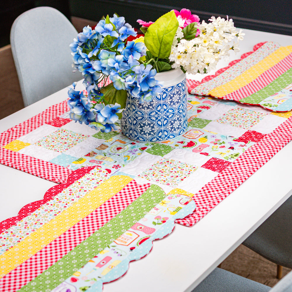 Colorful patchwork table runner on a white table with floral decorations.