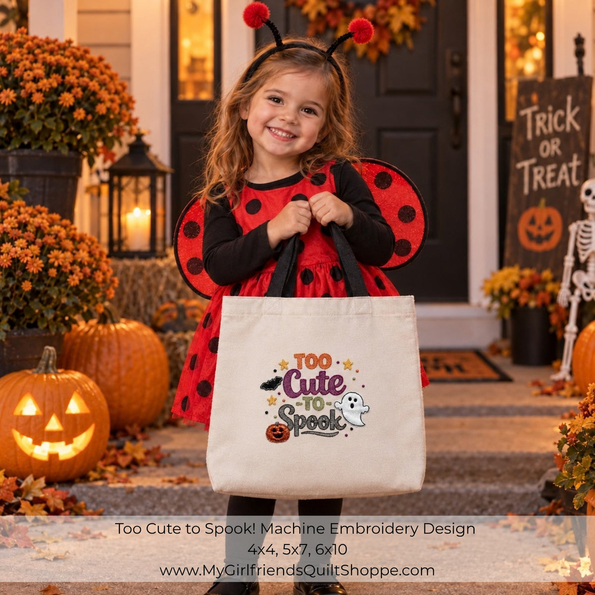A young girl in a ladybug costume stands on a front porch holding a large cream canvas tote bag with a colorful 'Too Cute to Spook!' embroidery design. Pumpkins, orange flowers, a Halloween sign, and a skeleton decoration are visible around her.
