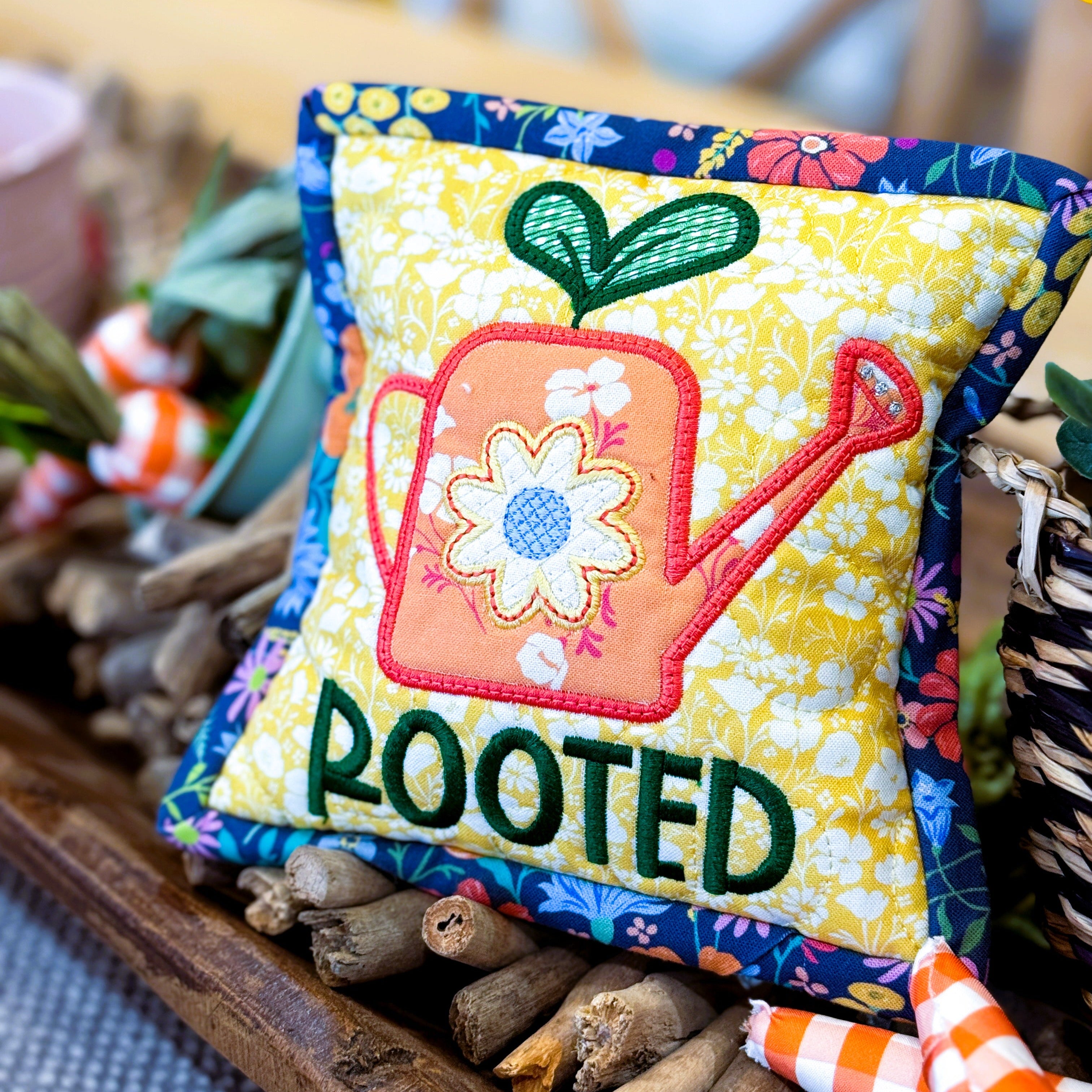 Decorative pillow with 'ROOTED' text and gardening-themed design on a table.
