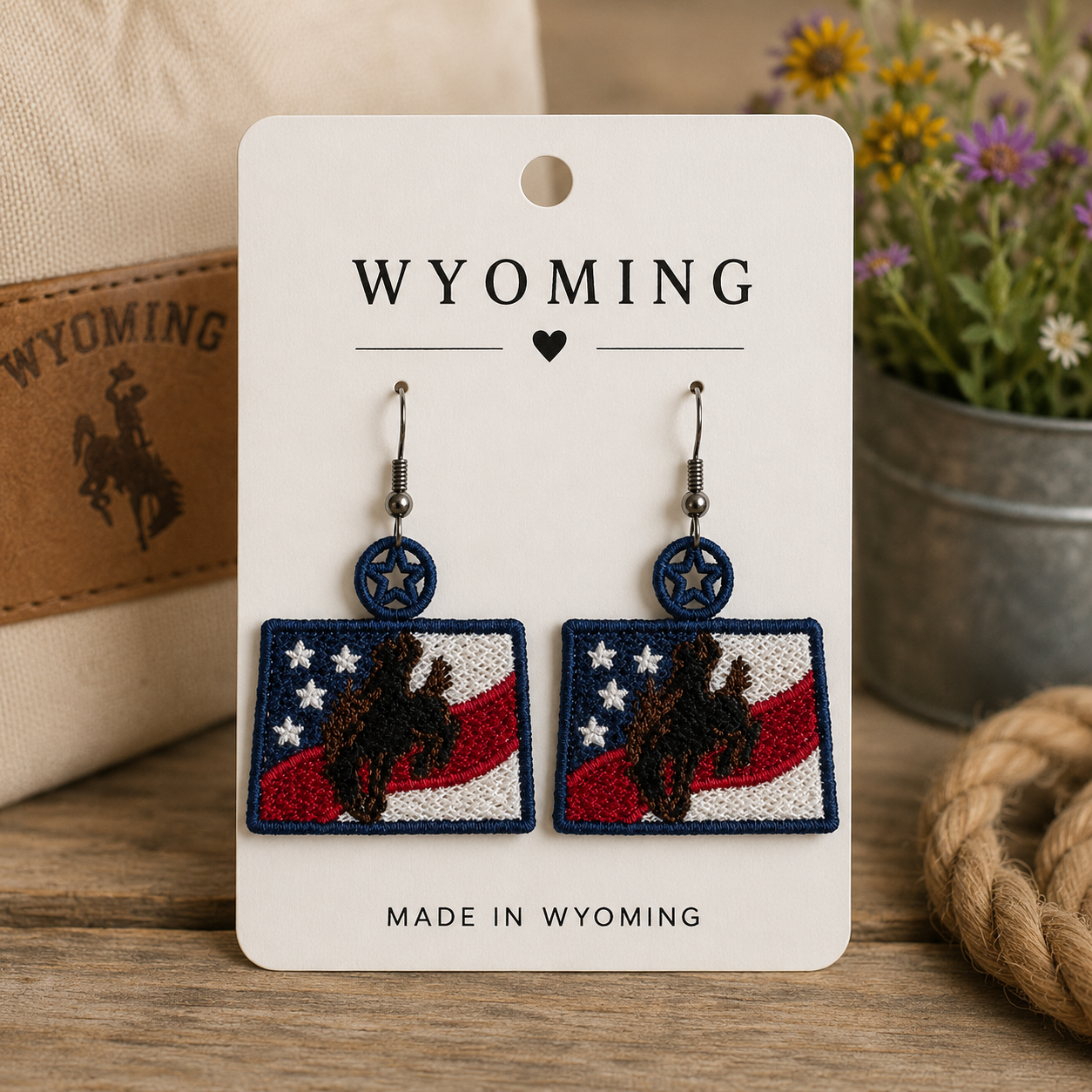 Wyoming-themed earrings on a card with a cowboy hat and flowers in the background