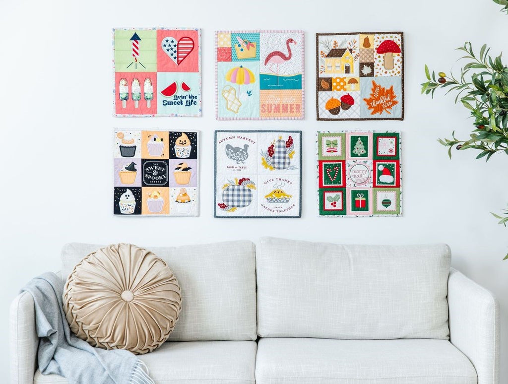 Mini Quilts Vol. 2 hanging on a wall above a couch 