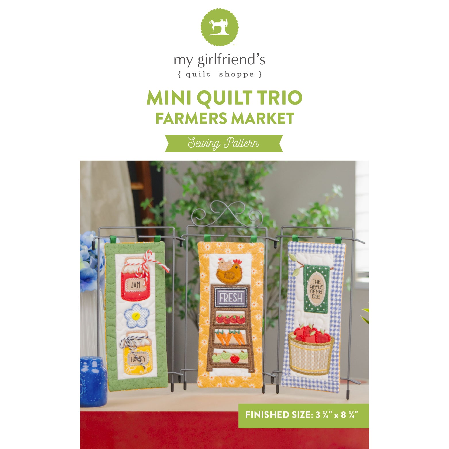 Sewing pattern cover for 'Mini Quilt Trio - Farmers Market' by my girlfriend's quilt shoppe, showing three completed mini quilts displayed on a stand with a green banner at the bottom indicating finished size of 3 1/2 x 8 1/2 inches.