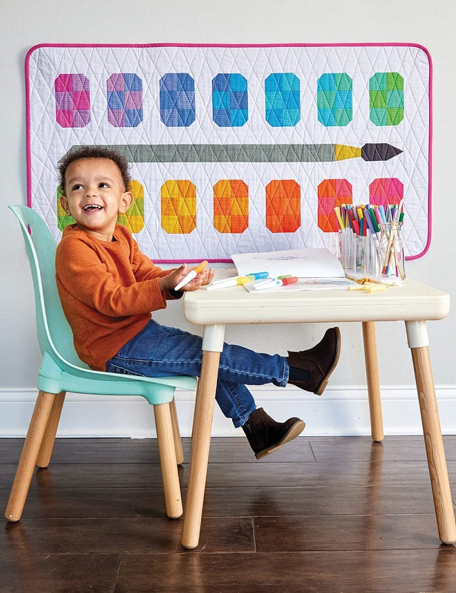 watercolor pallet quilt hanging on the wall behind a child