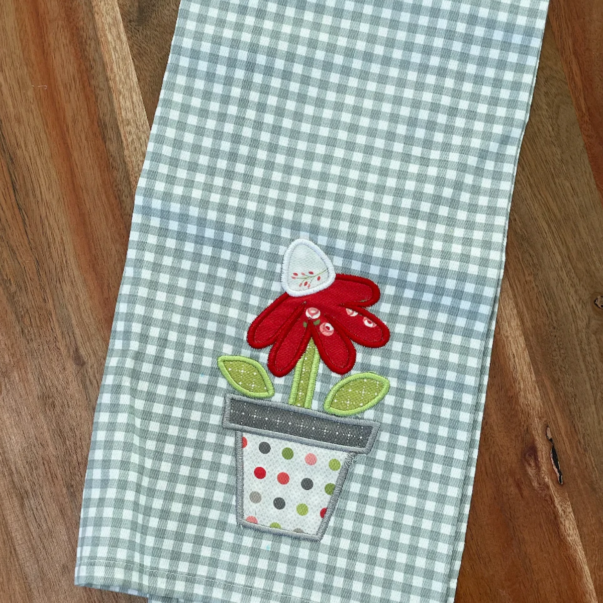 A tea towel with an embroidered applique flower in a pot.