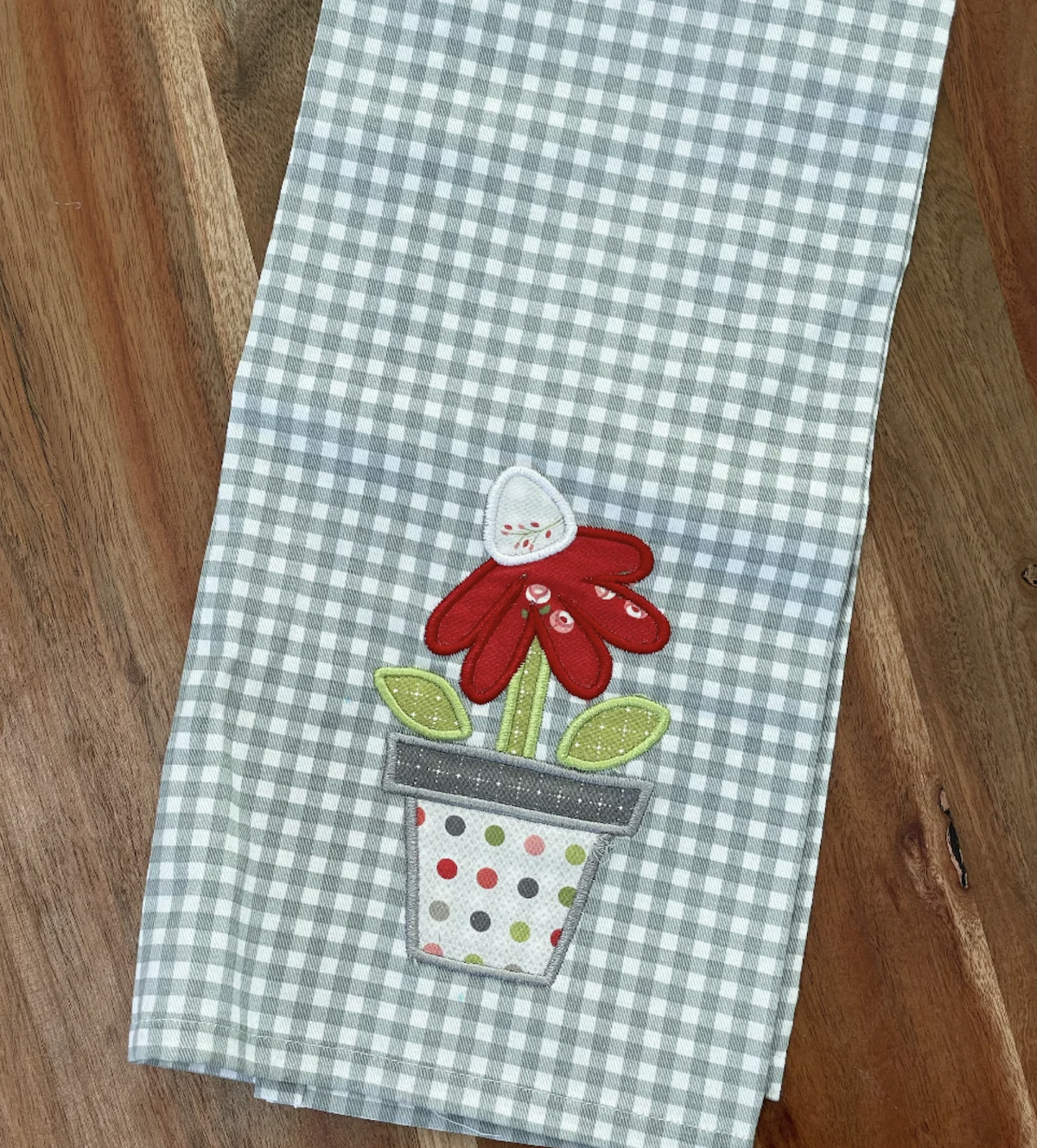 A tea towel with an embroidered applique flower in a pot.