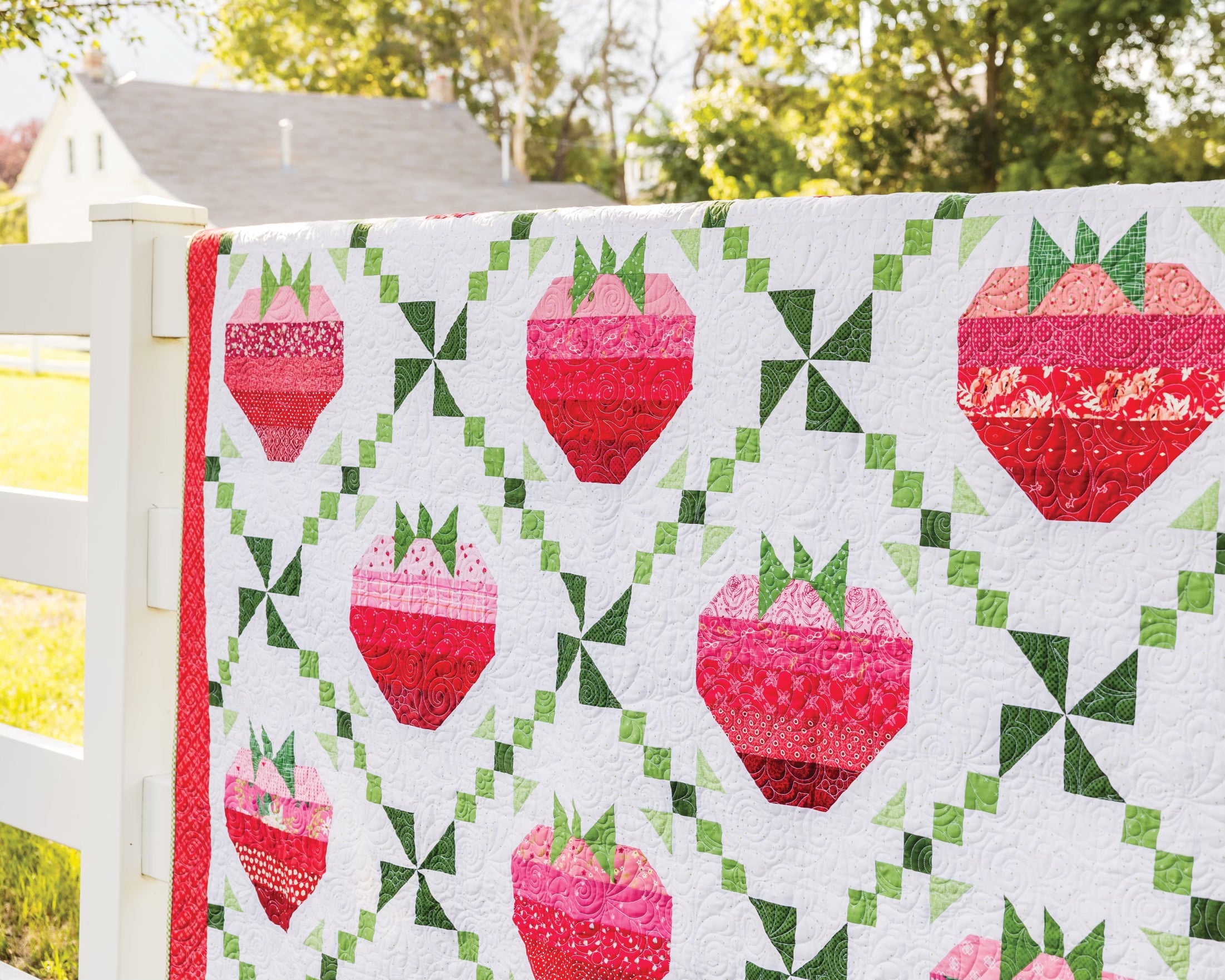 Quilt with pink and red strawberries hanging on a fence 