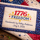 Quilted item with '1776 Freedom' label and embroidered text, held by a hand.