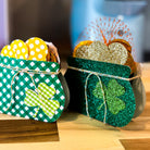 Two decorative pots with shamrock designs filled with colorful polka dot and glittery hearts on a wooden surface.