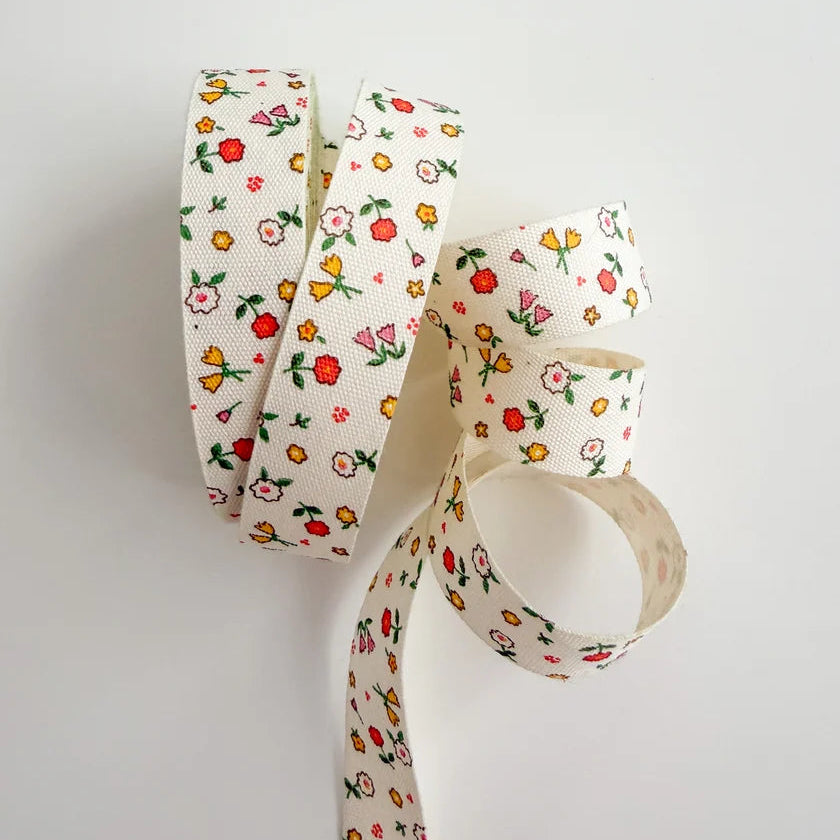 A roll of cream-colored grosgrain ribbon with a colorful floral print, unrolled into loops against a plain white background.