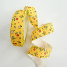 A roll of yellow grosgrain ribbon with a colorful floral pattern, shown coiled and unrolled on a plain white background.