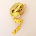 A roll of yellow patterned washi tape with a small floral and insect design, unrolled into a long ribbon on a light cream background.