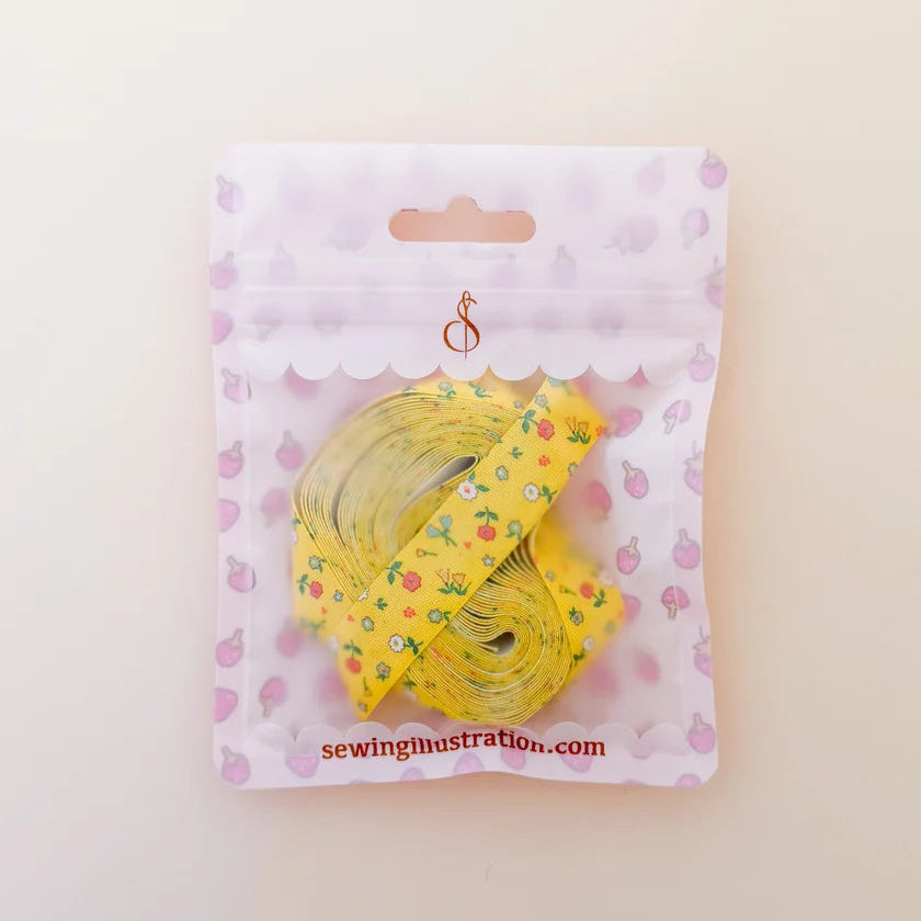 A yellow measuring tape roll with a small floral pattern, packaged in a white and pink strawberry-themed zip pouch. The brand name 'sewingillustration.