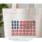 White tote bag with red and blue sewing machine pattern resembling an American flag, with a plant in the background.