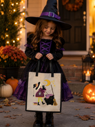 A young girl in a black and purple witch costume holds a canvas trick-or-treat bag decorated with a witch, cat, and cauldron illustration. She is standing outdoors in front of a house decorated for Halloween with pumpkins, flowers, and warm string lights.