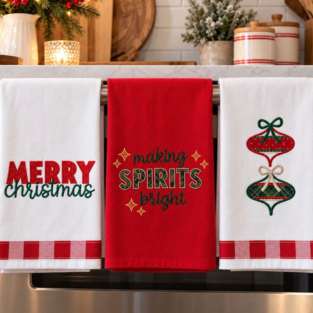 Three Christmas kitchen towels hanging on a metal rack in a kitchen setting. The left towel is white with 'MERRY christmas' embroidered in red and green, the center towel is red with 'making SPIRITS bright' in green and gold, and the right towel is white with a red and green ornament design and a red gingham band.