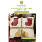 A quilted Christmas-themed throw pillow shown on a white background with branding text above reading 'my girlfriend's quilt shoppe' and 'A WINDOW TO CHRISTMAS: BY THE FIRE' plus 'Sewing Pattern.' The pillow has a patchwork design with four red stocking shapes, cream quilted sections, green floral trim, and dark green border details.