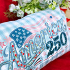 Decorative pillow with 'America 250' text and American flag design on a red background.