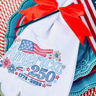 Embroidered towel with 'America 250' design and red ribbon on a decorative plate.