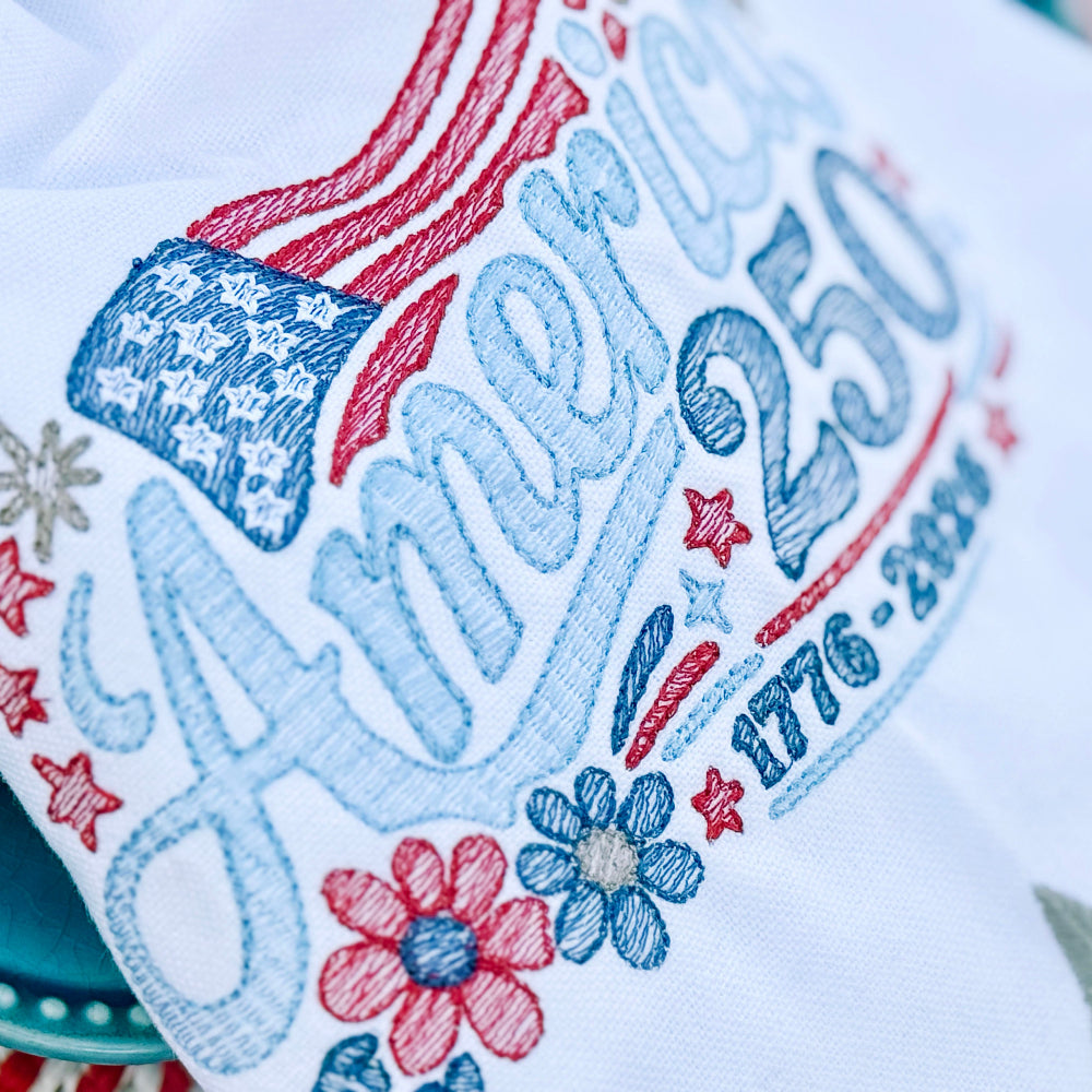Embroidered towel with 'Happy 250th America' text and decorative elements on a white background.