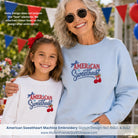 Two people wearing 'American Sweetheart' embroidered sweatshirts with festive background
