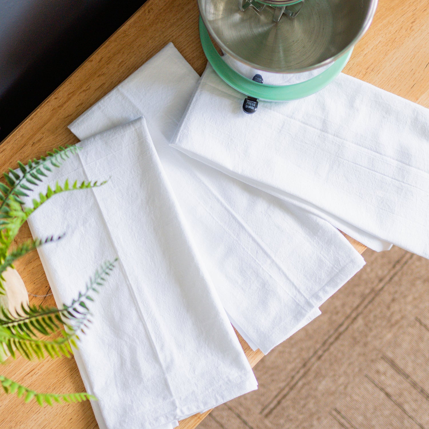 White napkins on a wooden surface with a plant and small appliance.