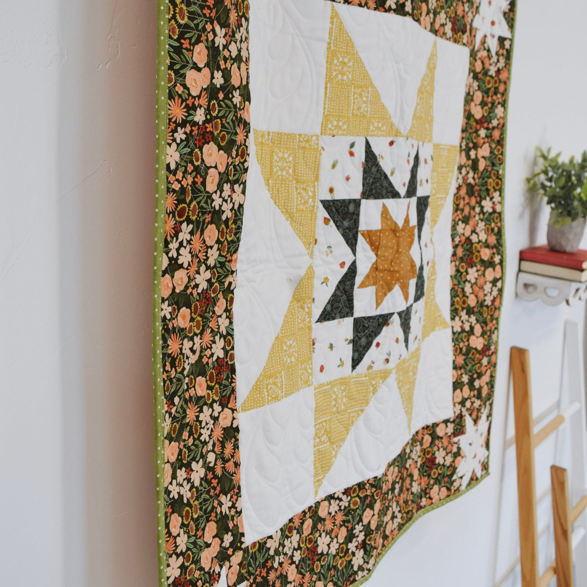 Quilt with star pattern hanging on a rack against a white wall.